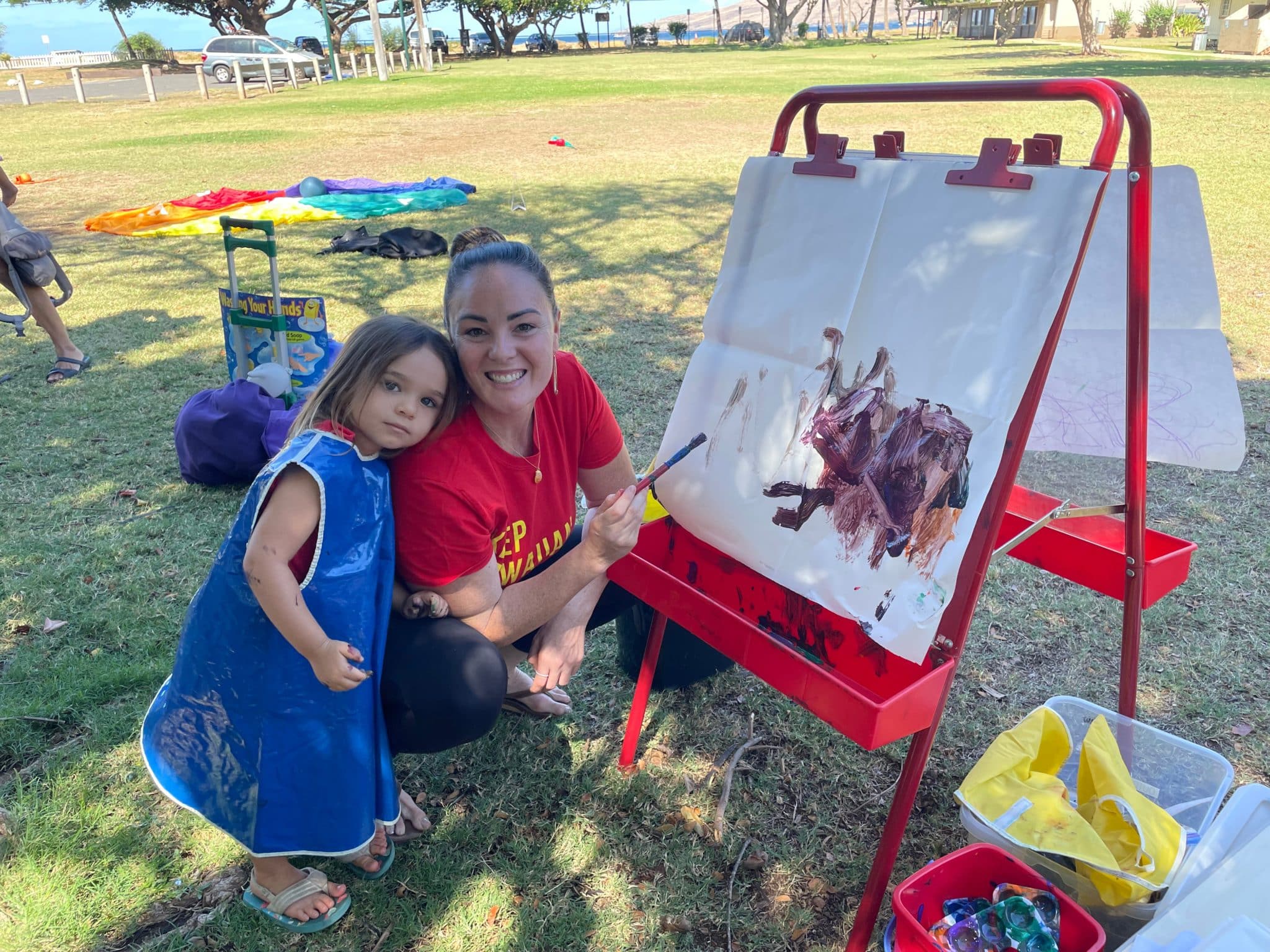 Little girl and her mother pose next to an easel containing the little girl's artwork.